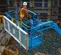 Top view of a blue boom lift platform with safety railing, operator wearing safety gear, elevated on a construction site.
