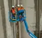 Front angled view of three workers in safety gear on a blue boom lift working on a concrete wall on an outdoor work zone.