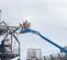 Side view of three workers on a blue boom lift platform looking at infrastructure outdoors on a construction site.