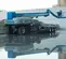 Side view of blue Genie boom lift with extended arm and worker on the platform positioned outdoors on wet ground.