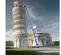Wide side view of a blue Genie boom lift with fully extended arm in front of the Tower of Pisa.