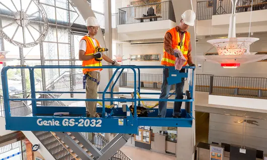 Two workers on a scissor lift inside of a building