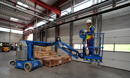 Trabajador en una brazo de elevación eléctrico dentro de un almacén